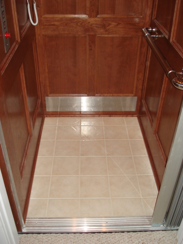 open elevator with wood panelling, polished handrail, and tile floor